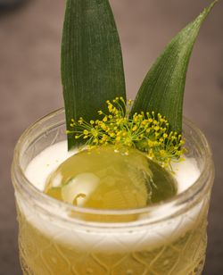 Mediterranean restaurant drink with foam, green jelly sphere, and two large green leaves topped with small yellow flowers.