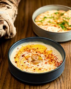 Creamy hummus seasoned with spices and olive oil, served with pita bread on a wooden table in a Mediterranean restaurant.