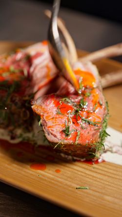 Grilled lamb chops seasoned with herbs and sauce, served on a wooden plate at Mēdüzā Mediterrania New York.
