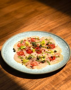 Mediterranean-style carpaccio with thinly sliced fish, cherry tomatoes, capers, and fresh herbs on a gray plate