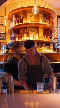 Bar area in a fine dining restaurant with a bartender, bottles displayed on a circular shelf, and warm lighting