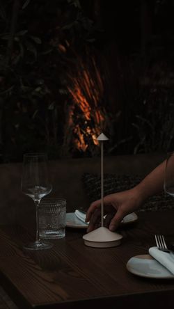 Table set for fine dining with wine glass, water glass, and hand near a lit table candle in a Mediterranean restaurant.
