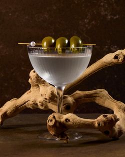 Cocktail glass with three green olives on a skewer, set against a rustic wooden branch and dark background