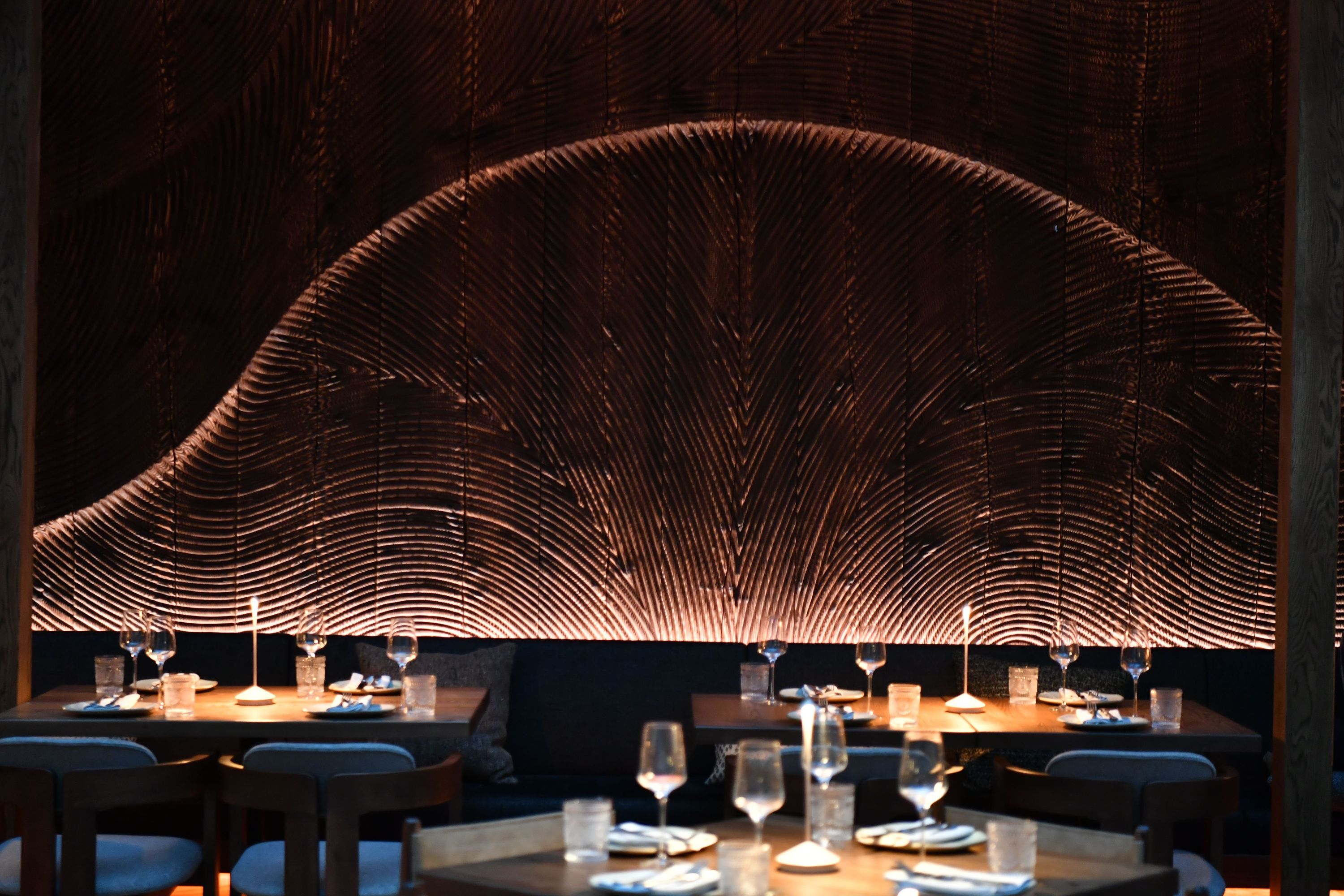Fine dining restaurant interior with wooden tables, elegant glassware, and decorative textured wood wall panels.