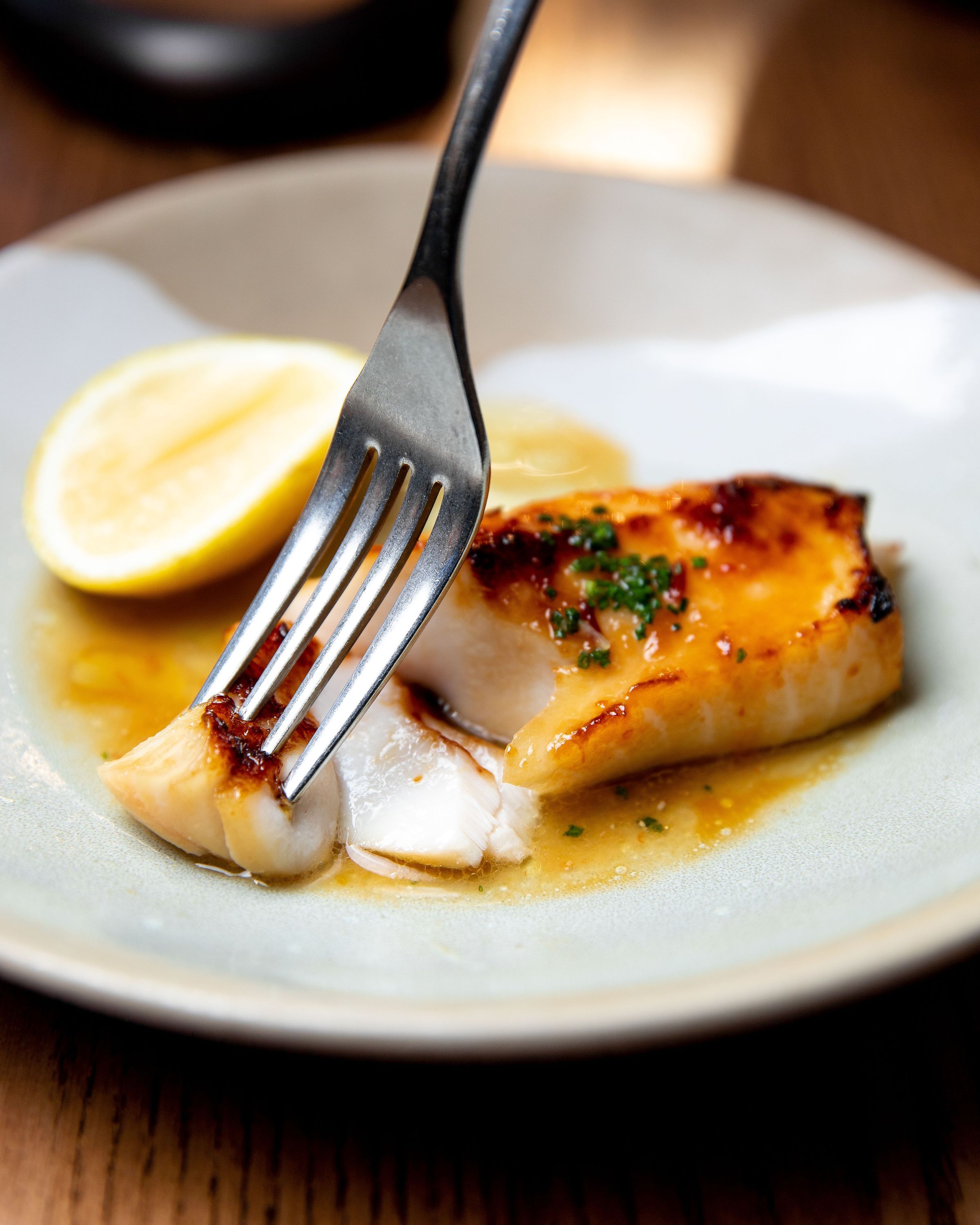 Grilled fish dish with sauce and lemon wedge, served on a ceramic plate at a fine dining restaurant.