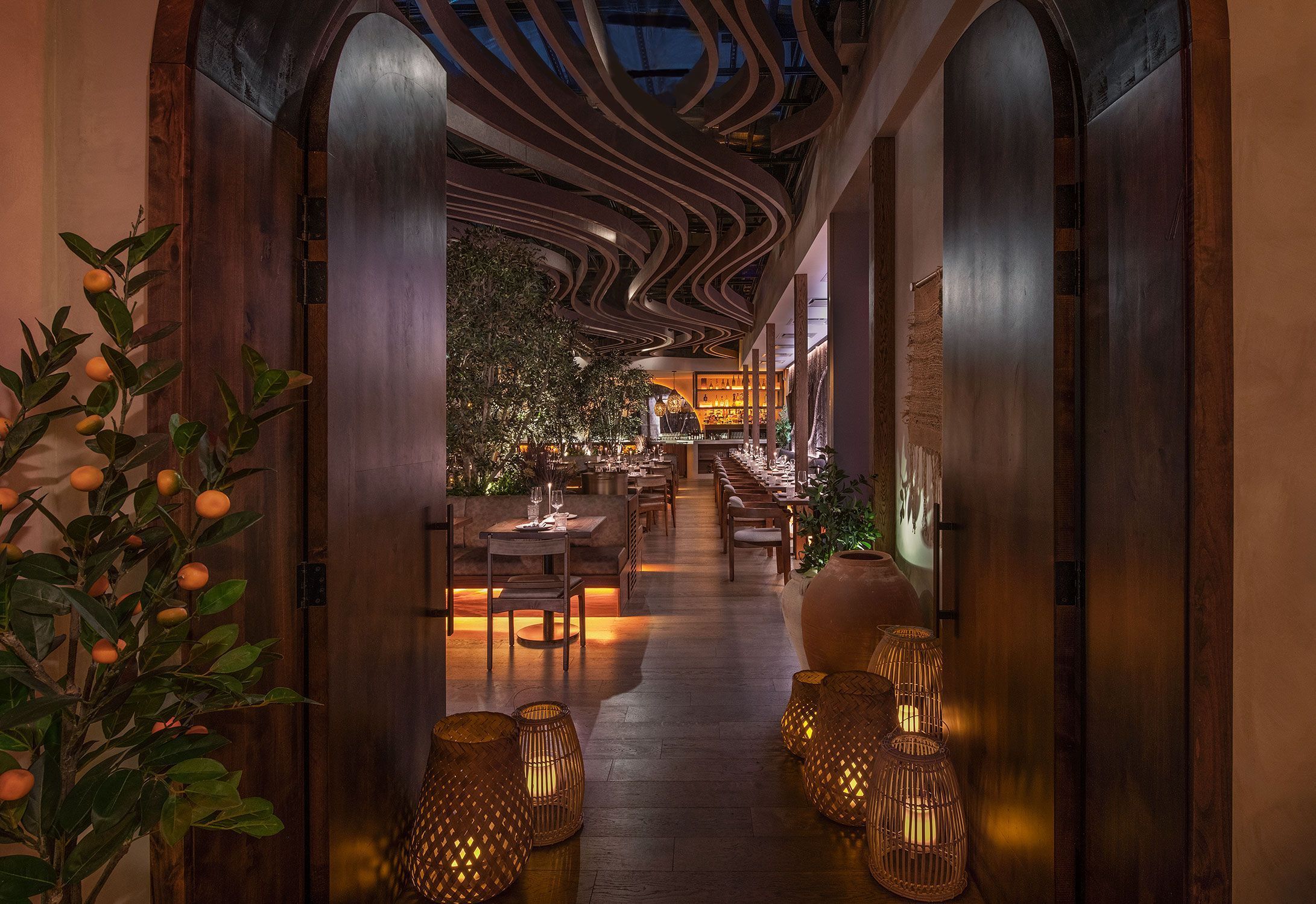 Mediterranean fine dining restaurant interior with ambient lighting, wooden tables, and decorative plants and lanterns.