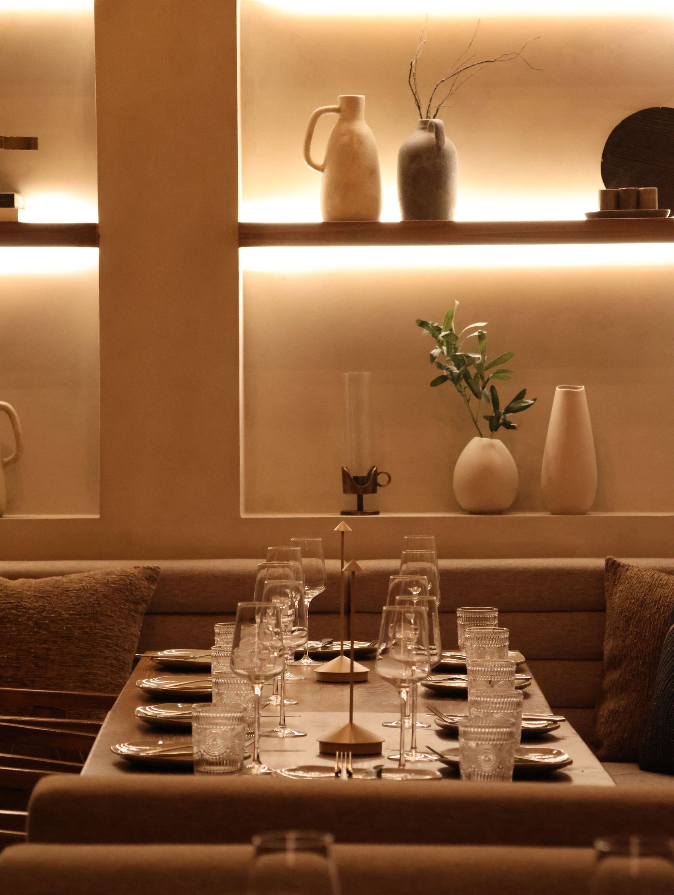 Elegant fine dining setting with neatly arranged glassware and modern ceramic decor on illuminated shelves.